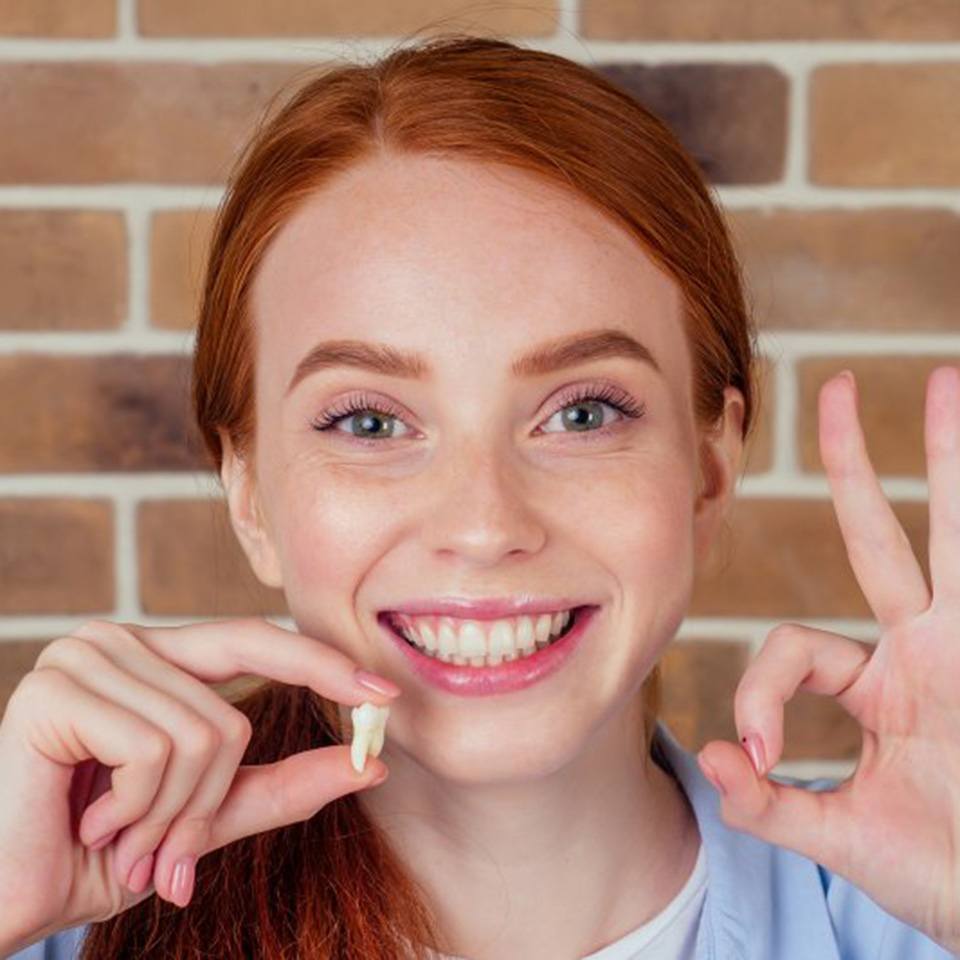 Woman holding her wisdom tooth and smiling 