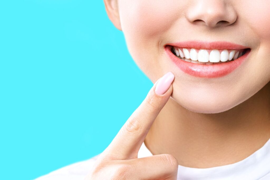 Nose-to-neck image of woman pointing to her smile with pink nail