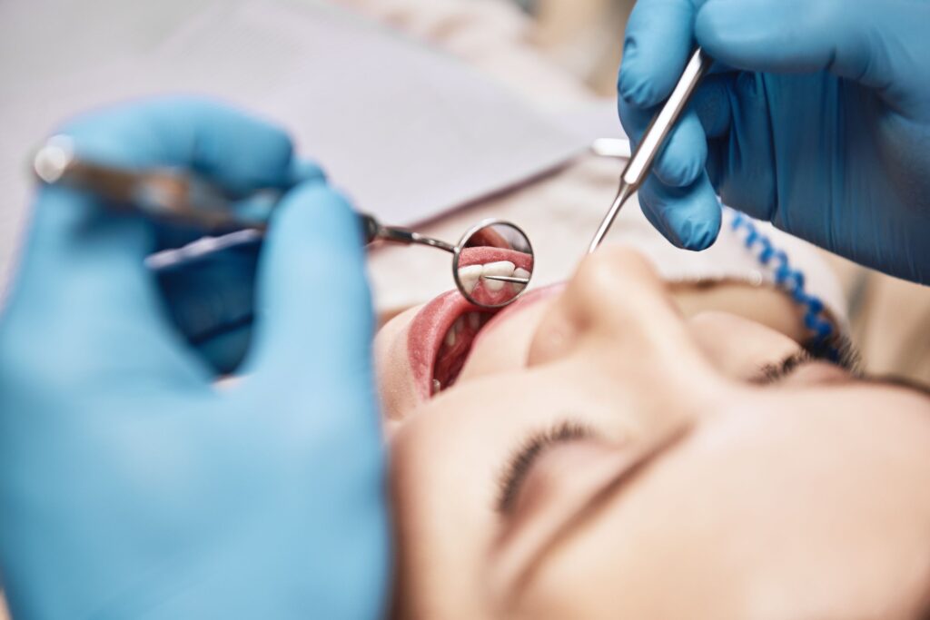 Blue-gloved hands examining woman's teeth